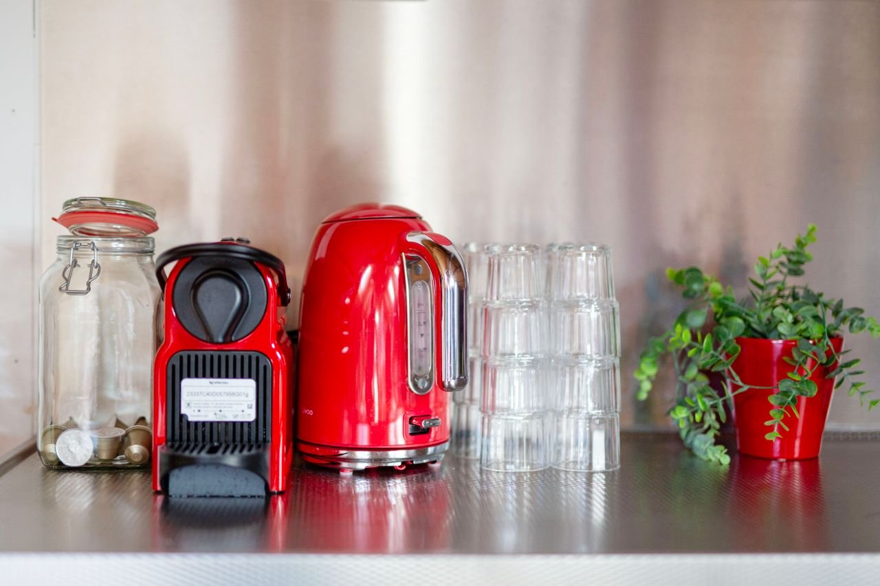 Services Stylish kitchen set-up with red appliances and greenery on a steel counter. Perfect for coffee lovers.